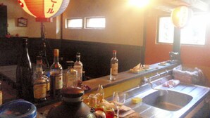 Zona de bar con botellas, vasos y un lavamanos.