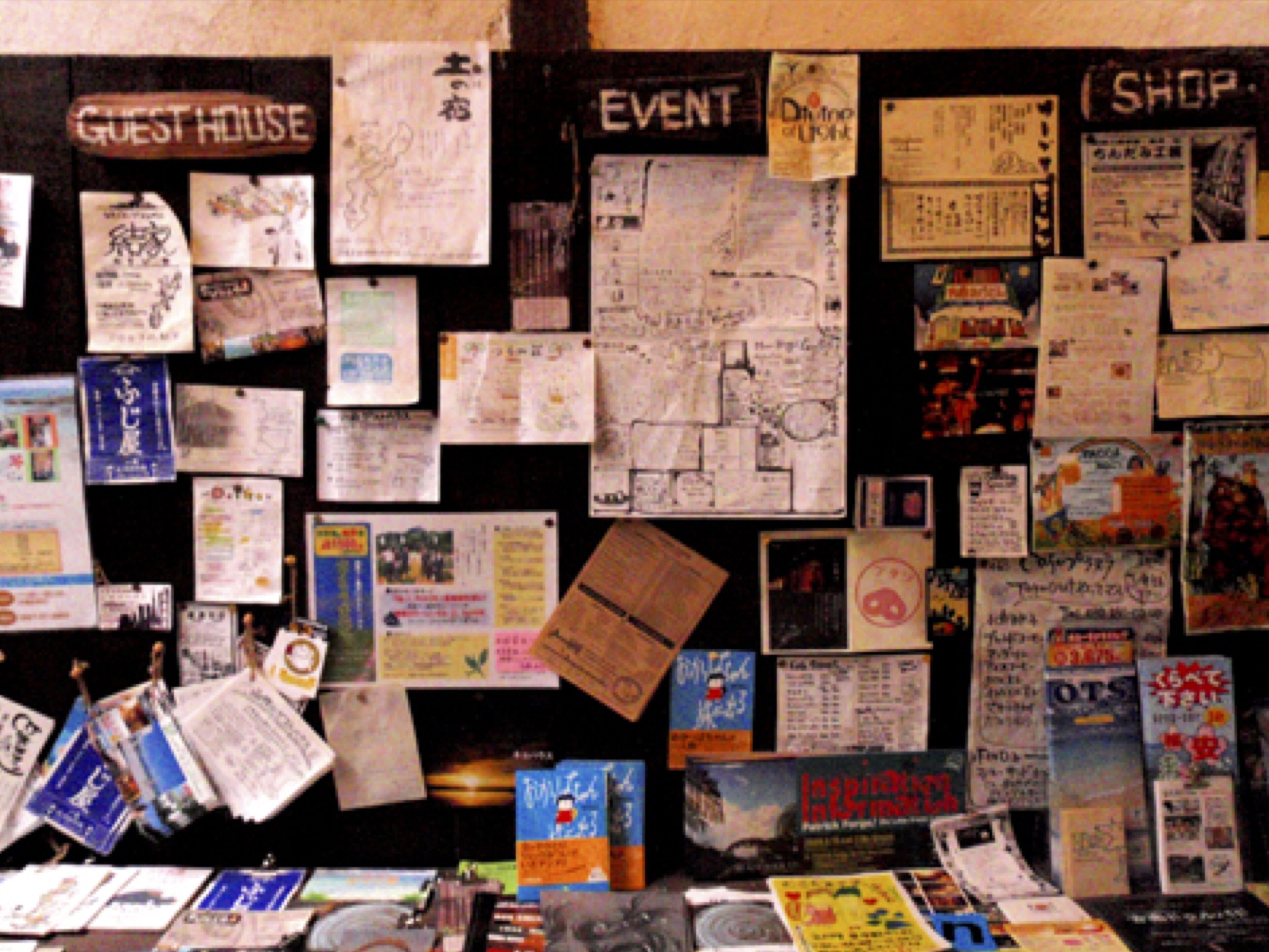 A bulletin board with various notices and flyers, including a 'Guest House' sign, an 'Event' notice, and a 'Shop' sign.