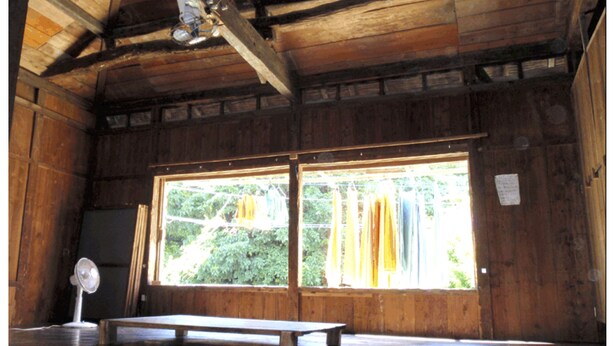 Una habitación de madera con un ventanal grande, un banco y un ventilador.