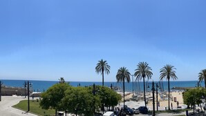 A coastal promenade with palm trees, a beach, and a clear blue sky. - RIBERA PETIT BY BLAUSITGES Small apartment with superb sea views in Sitges. (SITGES)