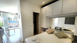 A hotel room with a bed, a TV, and a view of the beach. - RIBERA PETIT BY BLAUSITGES Small apartment with superb sea views in Sitges. (SITGES)