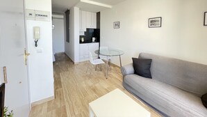 A modern living room with a grey sofa, a small round glass table, and a white coffee table. There is a kitchen area with white cabinets and a small dining table. - RIBERA PETIT BY BLAUSITGES Small apartment with superb sea views in Sitges. (SITGES)