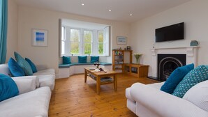 Een woonkamer met witte banken, een houten salontafel, een open haard en een tv die erboven is bevestigd.