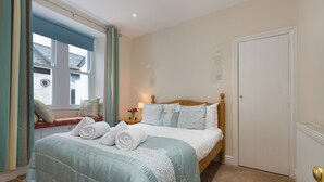 Een net opgemaakt bed met een blauw-witte sprei, een houten hoofdbord en een raam met gordijnen.