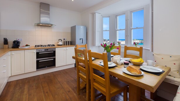 Een moderne keuken met witte kasten, een houten eettafel en uitzicht op de zee door grote ramen.