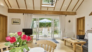 A dining area with a wooden table set for two, a vase with red roses, and a television in the background. - Kipper Cottage  -  a bungalow that sleeps 4 guests  in 2 bedrooms (Ryde)
