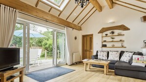 A spacious living room with a large TV, wooden furniture, and a view through glass doors to an outdoor area. - Kipper Cottage  -  a bungalow that sleeps 4 guests  in 2 bedrooms (Ryde)