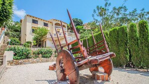 A rustic outdoor area with a large, rusted metal wheel structure, a stone wall, and a building with a balcony in the background. - Kanky 6 - modern, well-equipped villa with private pool in Benissa coast (Benissa)