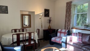 A cozy living room with a dining table, chairs, a sofa, a coffee table, and a window with curtains. - The Maid's House, Carmichael Country Cottages. 4 star comfortable cottage on rural Estate (Biggar)