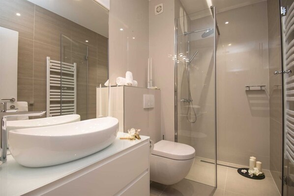 A modern bathroom with a large white sink, a toilet, and a glass-enclosed shower.