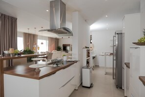 Een moderne keuken met een centraal eiland, witte kasten, roestvrijstalen apparatuur en een zithoek met een bank en tafel.