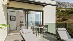 A balcony with two lounge chairs, a small table with a wine glass, and a view of a mountainous landscape.