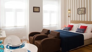 A hotel room with a bed, two armchairs, a dining table with plates and glasses, and a large window. - Porto Náutico & Spa 3 | Studio Deluxe (Porto)