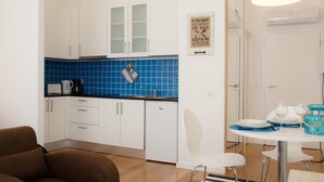 A modern kitchen with white cabinets, a blue backsplash, and a dining area with a table set for two. - Porto Náutico & Spa 3 | Studio Deluxe (Porto)