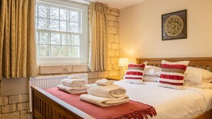 Ein Hotelzimmer mit großem Fenster, einem Bett mit weißer Bettwäsche und roten und weißen Streifen-Kissen, einem Holz-Kopfteil und einem Heizkörper unter dem Fenster.