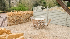 A patio with a stone wall, a wooden table and chairs, and a white lattice gate. - A sudeley castle cottage that sleeps 4 guests  in 2 bedrooms (Cheltenham)