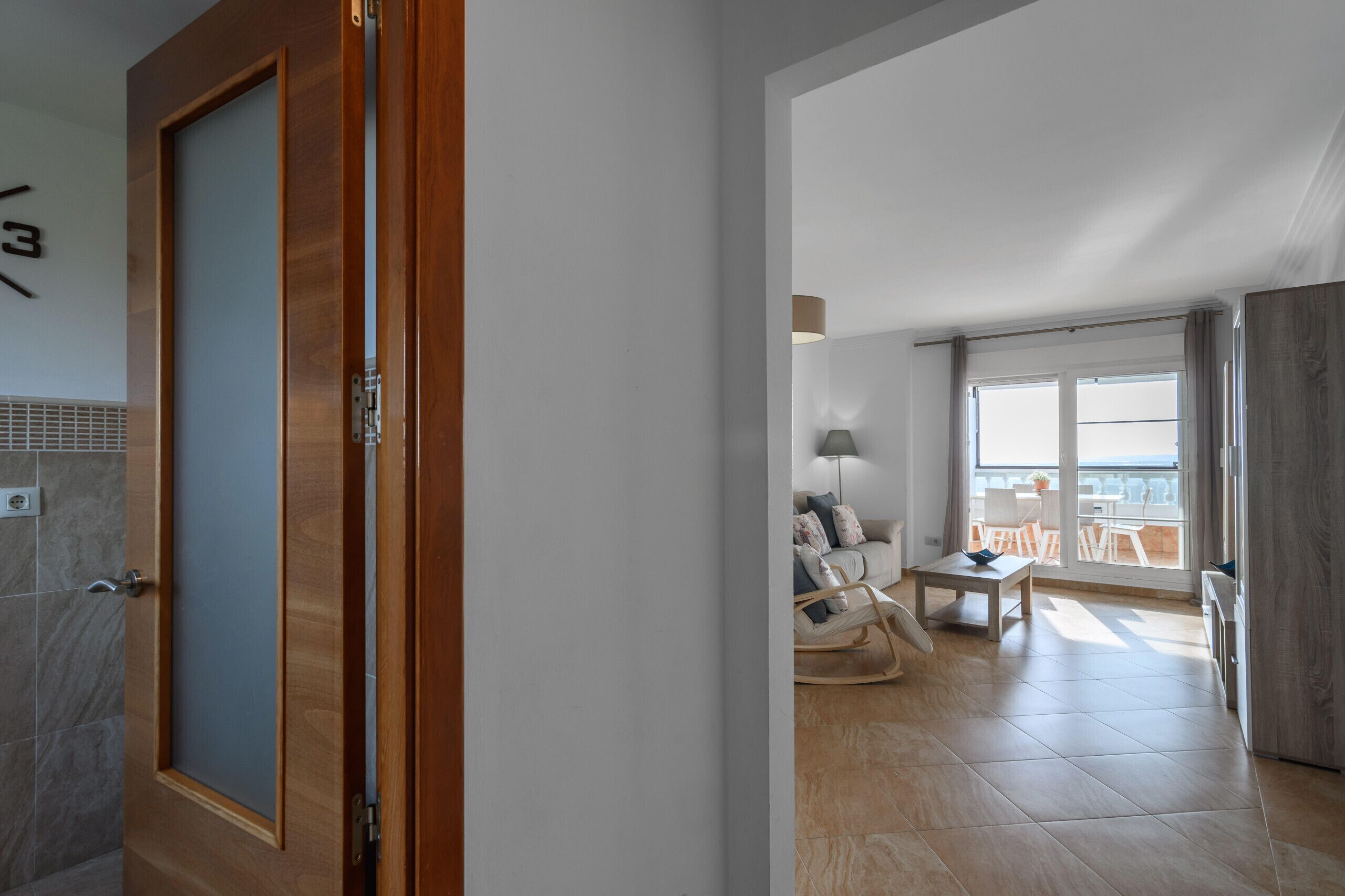 Un intérieur moderne avec une porte en bois, un balcon offrant une vue, un coin salon avec une table et une grande fenêtre.