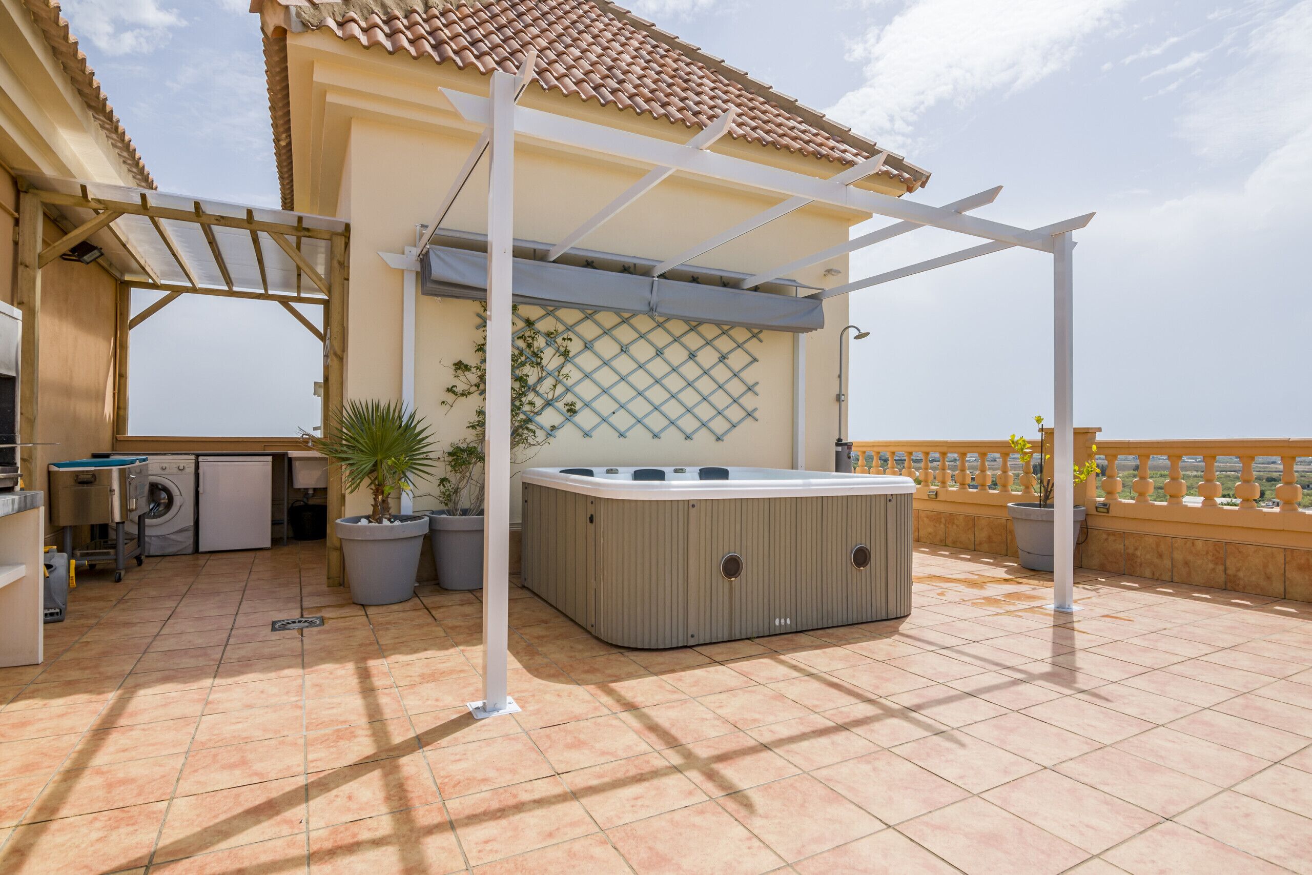 Un espacio exterior techado con jacuzzi, lavadora y plantas en macetas.
