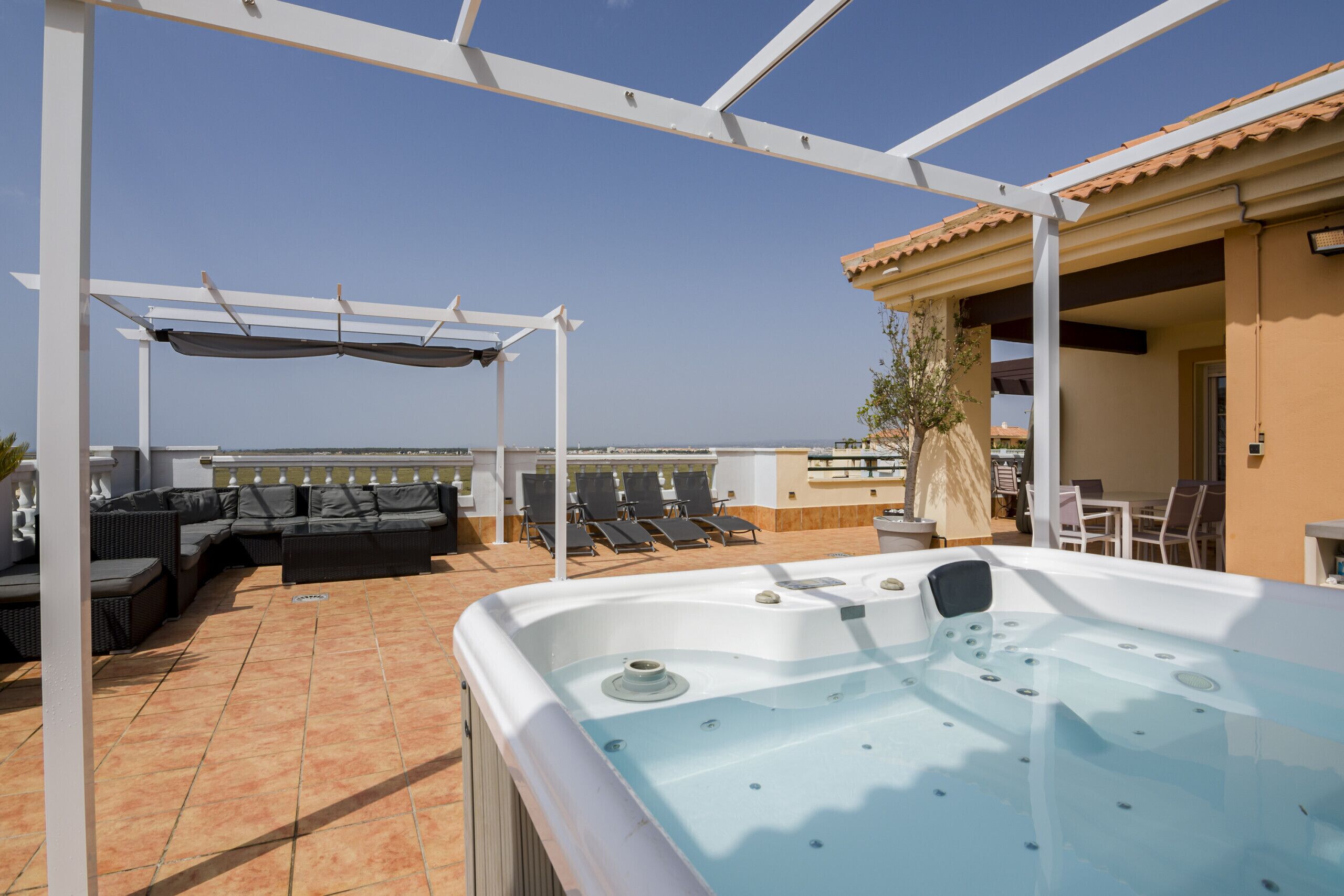En tagterrasse med jacuzzi, udendørs møbler og et pergolaoverdækket område.