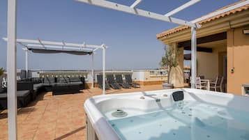 En tagterrasse med jacuzzi, udendørs møbler og et pergolaoverdækket område.