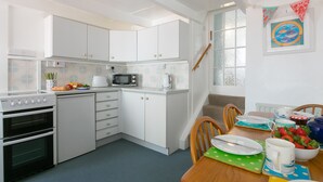 Une cuisine moderne avec des meubles blancs, un four à micro-ondes et une cuisinière. On y trouve une table à manger avec des chaises et un panier de fruits.