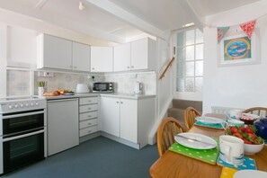 A modern kitchen with white cabinets, a microwave, and a stove. There is a dining table with chairs and a fruit bowl.