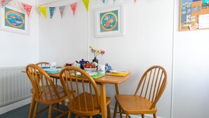Un coin repas avec une table et des chaises en bois, un tableau d’affichage où sont accrochées diverses notes et photos, et des fanions triangulaires colorés sur le mur.