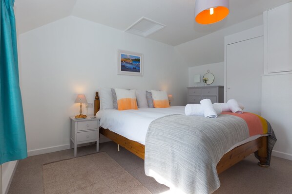 A bedroom with a bed, bedside tables, a nightstand, a painting, and a mirror.