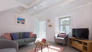 Un salon comprenant un canapé, un fauteuil, une table basse, un meuble pour la télévision et des œuvres d’art accrochées aux murs.