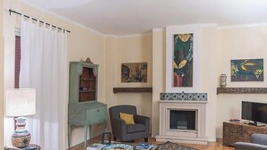 Un salon avec une cheminée, un meuble vert, un fauteuil gris et un téléviseur.