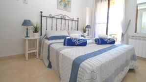 Quarto com duas camas, mesa de cabeceira com abajur, planta em vaso e janela com cortinas.
