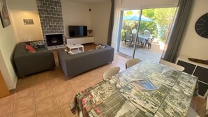 A living room with a fireplace, a sofa, a television, and a dining area with a table covered in a magazine. - Daró 3D 56 - 50m from the beach, with pool (Torroella de Montgri)