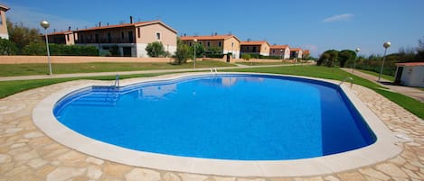 En swimmingpool med en kant av sten, omgiven av en välskött gräsmatta och en rad byggnader i bakgrunden.