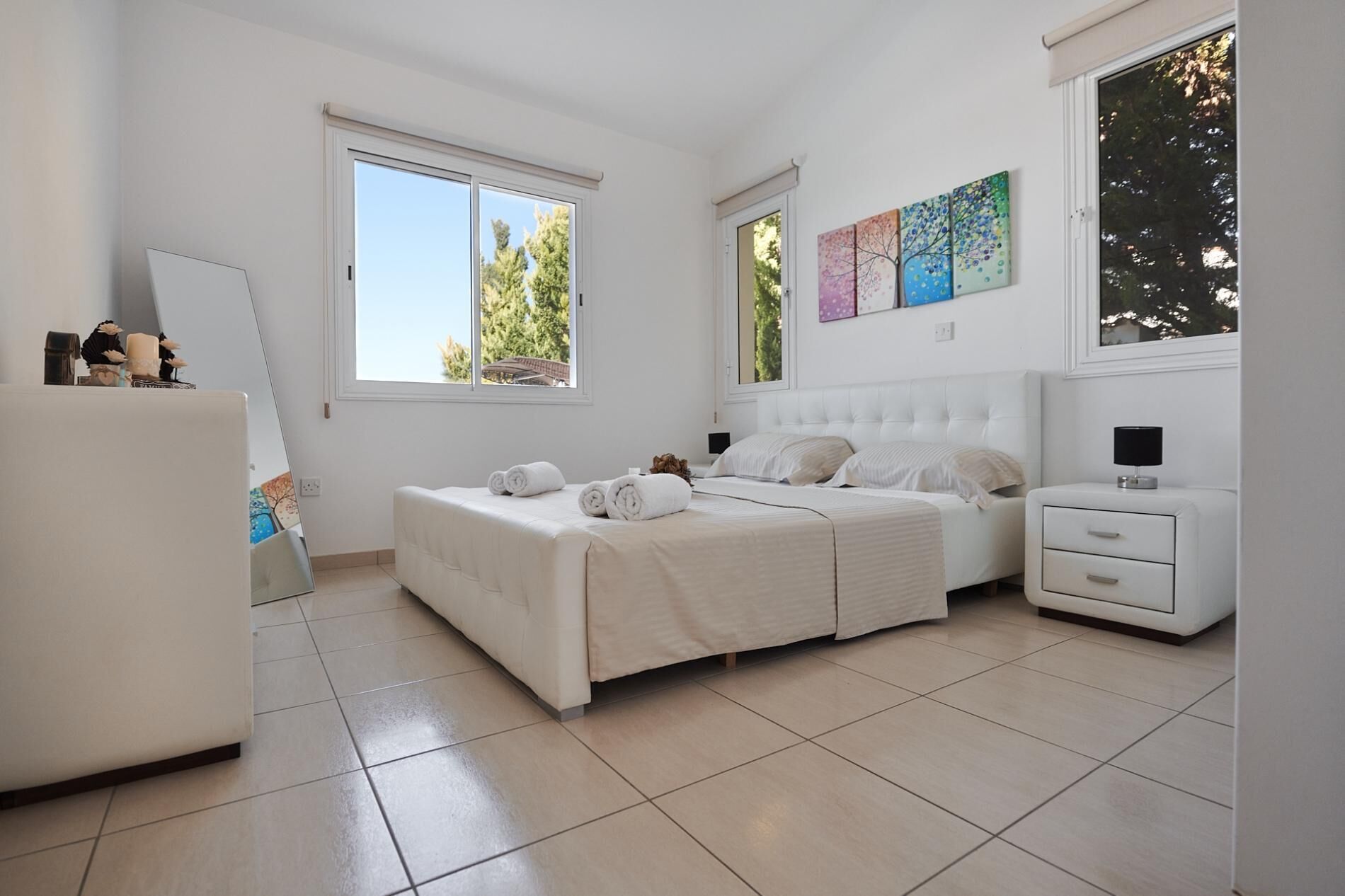 Une chambre à coucher comprenant un lit, deux tables de chevet, une commode et des œuvres d’art accrochées aux murs.