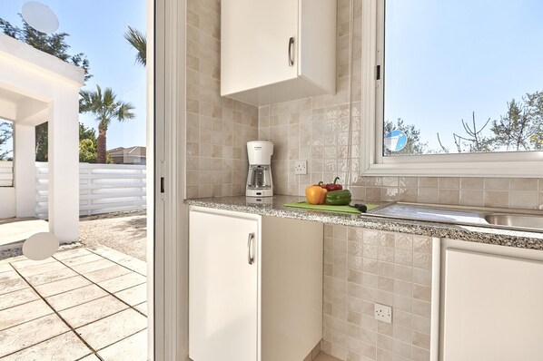 A kitchen with white cabinets, a coffee maker, and a window with a view of palm trees.