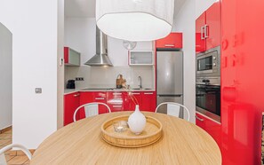 A modern kitchen with red cabinets, stainless steel appliances, a round wooden table, and white chairs.