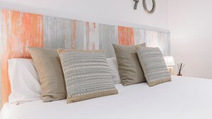Una cama con varias almohadas, una pared blanca y el número decorativo '70' en la pared.
