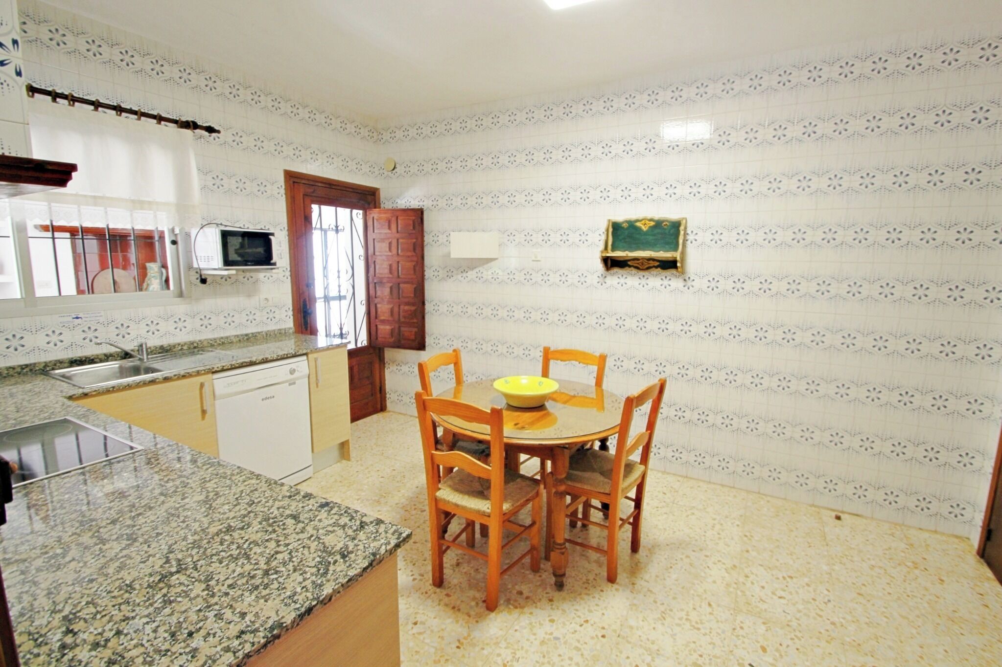 Cuina amb taulell de granat, taula de dinar de fusta i caires, microones i finestra amb porta.