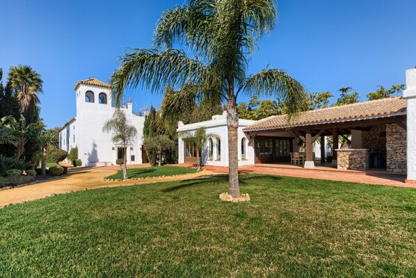 A white building with a bell tower, surrounded by palm trees and a well-maintained lawn.