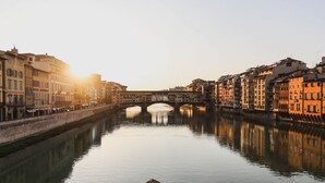A river with buildings on both sides, a bridge in the middle, and a calm water surface.