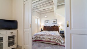A bedroom with a bed, a television on a cabinet, and a door leading to another room.