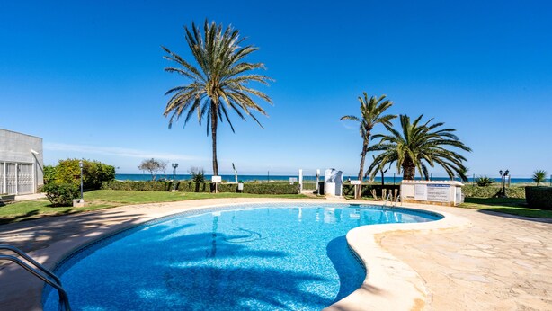 Une piscine à bord incurvé, entourée d’une terrasse en pierre et de palmiers, avec une vue sur l’océan en arrière-plan.