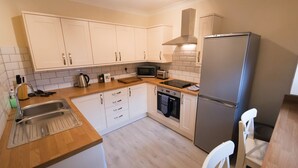 Ett modernt kök med vita skåp, en diskho i rostfritt stål, en mikrovågsugn, en brödrost, en diskmaskin och ett kylskåp.