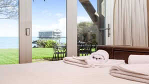 A bedroom with a large window overlooking a grassy area and a building across the water. - Beach Side -  a house that sleeps 8 guests  in 4 bedrooms (Bembridge)