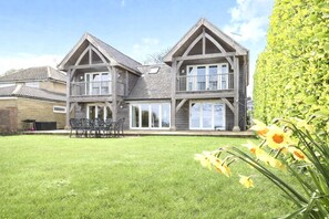 A two-story house with a balcony, a lawn, and a garden with daffodils.