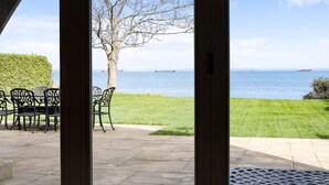A patio with a table and chairs, a lawn, and a view of the sea with ships in the distance. - Beach Side -  a house that sleeps 8 guests  in 4 bedrooms (Bembridge)