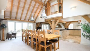 A spacious dining area with a high wooden ceiling, a balcony, and a kitchen in the background. - Beach Side -  a house that sleeps 8 guests  in 4 bedrooms (Bembridge)