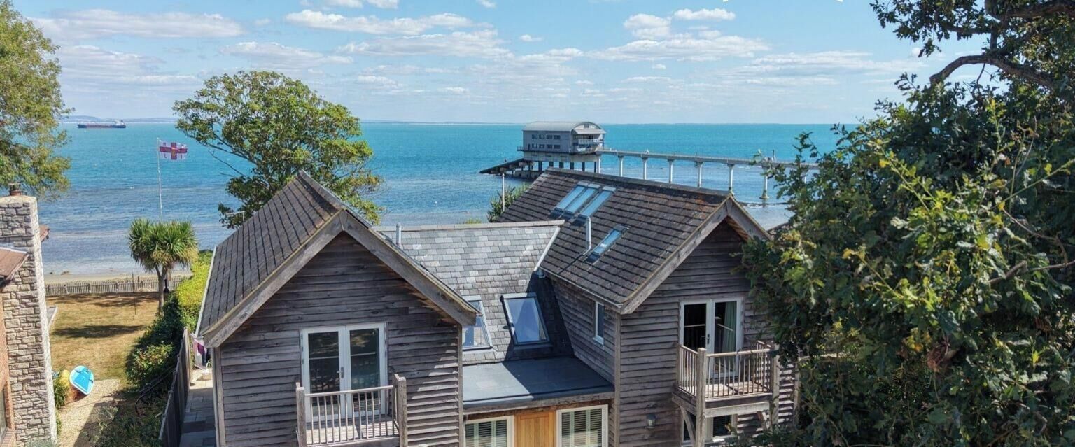Una casa de madera con balcón que da a un cuerpo de agua, un muelle y un barco a lo lejos.