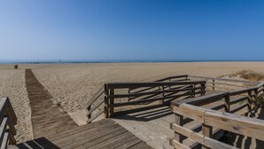 Un muelle de madera que conduce a una playa arenosa bajo un cielo azul despejado.