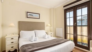 Habitación de hotel con cama, dos mesitas de noche, una lámpara de noche, ventana con vistas y un cuadro en la pared.